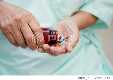 Asian elderly woman holding pill capsule drug in hand. 129660439