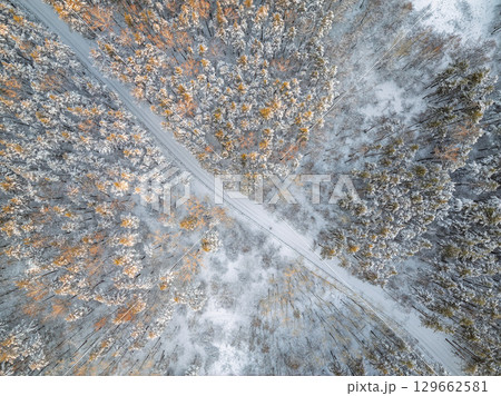 Aerial view of the road in the winter forest with high pine or spruce trees covered by snow. Driving in winter. Aerial view of the road in the winter forest with high pine or spruce trees covered by snow. Driving in winter. 129662581