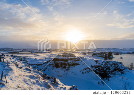 夕陽に染まる雪景色のディムボルギル溶岩地形と湖（アイスランド・ミーヴァトン） 129663252