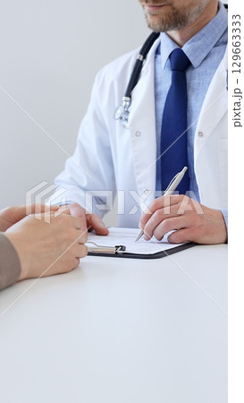 Unknown male doctor taking notes while listening to a female patient explaining her symptoms during a medical consultation in the clinic office. Medicine concept 129663333