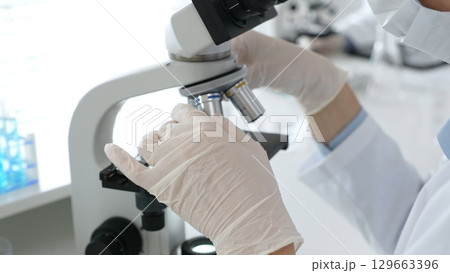 White gloved hands of scientist professional adjusting a microscope in a bright laboratory, emphasizing precision and focus in scientific research. Medicine, healthcare and science concept 129663396