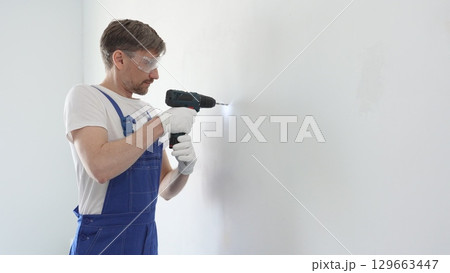 Skilled worker drilling hole in white wall, wearing protective gear during home improvement project with cordless power tool Skilled worker drilling hole in white wall, wearing protective gear during home improvement project with cordless power tool 129663447