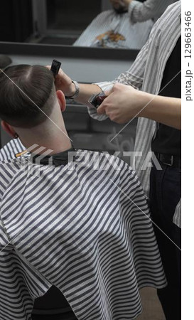 Professional barber grooming client's hair using electric clipper, delivering precise cut with skill in contemporary salon setting 129663466