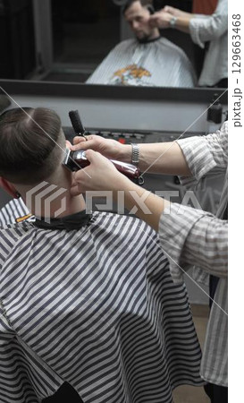 Professional barber grooming client's hair using electric clipper, delivering precise cut with skill in contemporary salon setting 129663468