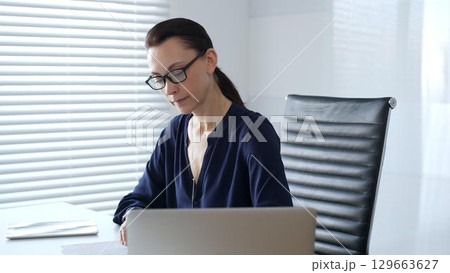 Businesswoman reviewing accounting documents while calculating financial data in modern office setting. Business people concept Businesswoman reviewing accounting documents while calculating financial data in modern office setting. Business people concept 129663627