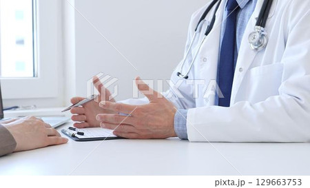 Adult doctor gesturing with hands while explaining diagnosis to patient during medical consultation in hospital office, healthcare and medical concept. Medicine concept Adult doctor gesturing with hands while explaining diagnosis to patient during medical consultation in hospital office, healthcare and medical concept. Medicine concept 129663753