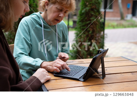 The granddaughter teaches the grandmother to use the tablet . 129663848