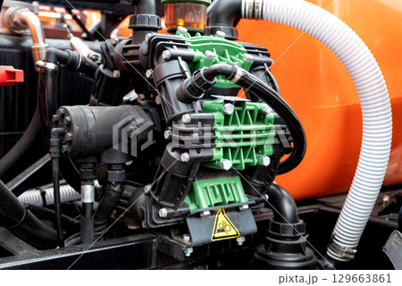 Close-up of industrial pump with green and black components, orange background. Close-up of industrial pump with green and black components, orange background. 129663861