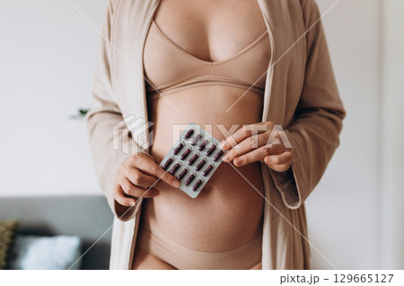 belly of pregnant woman and vitamin pills in the hand. Pregnant woman taking vitamins and minerals at home. Pregnant girl monitors their health. Medicine banner 129665127