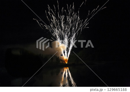 Celebration features colorful fireworks reflecting over calm lake during summer night Celebration features colorful fireworks reflecting over calm lake during summer night 129665188