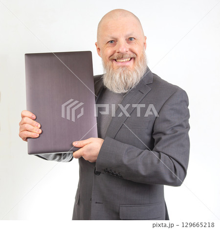 Smiling man in a suit presenting a sleek object against a plain background Smiling man in a suit presenting a sleek object against a plain background 129665218