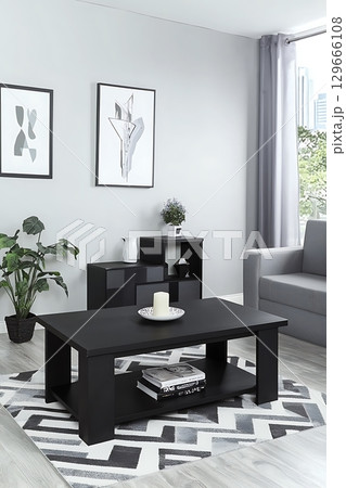 A black coffee table with a white plate and candle on it sits in a living room 129666108