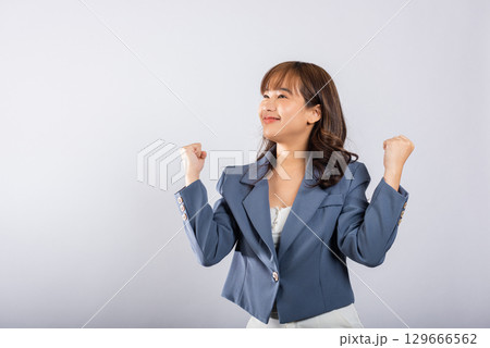 Portrait of a successful Asian business woman wearing a suit in a cheerful profile, raising her fists with a smile. Studio shot isolated on white, expressing triumph and excitement Portrait of a successful Asian business woman wearing a suit in a cheerful profile, raising her fists with a smile. Studio shot isolated on white, expressing triumph and excitement 129666562