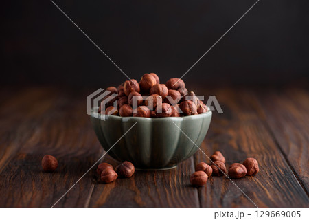 Hazelnuts in a bowl on a dark wooden background. Front view 129669005