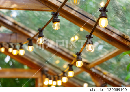 Rustic garland with lamp blulb lanterns glowing under of wooden celling, home decor, illumination 129669160