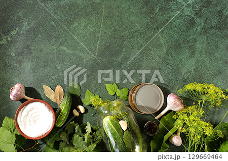 Homemade pickling recipe, cucumbers and pickling ingredients, Pickled cucumbers in jars with garlic and dill on wooden kitchen table, rustic style, home canning concept 129669464