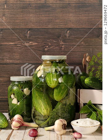 Pickled cucumbers in jars with garlic and dill on wooden kitchen table, rustic style,Homemade pickling recipe, cucumbers and ingredients for pickling, home canning concept 129669472