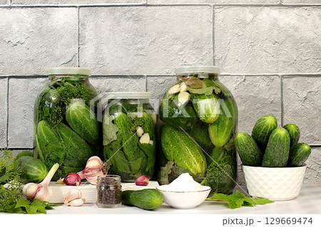 Pickled cucumbers in jars with garlic and dill on wooden kitchen table, rustic style,Homemade pickling recipe, cucumbers and ingredients for pickling, home canning concept 129669474