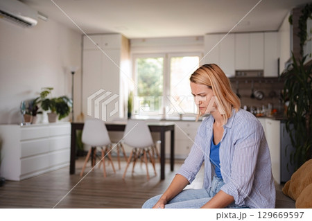 Sad woman sitting on sofa at home feeling depressed Sad woman sitting on sofa at home feeling depressed 129669597