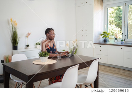 Focused Young Woman Working From Home on Laptop at Dining Table 129669616