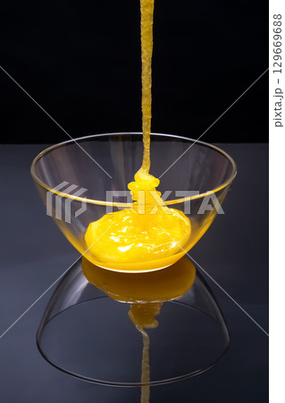 Viscous yellow substance being poured into a clear glass bowl on a dark surface 129669688