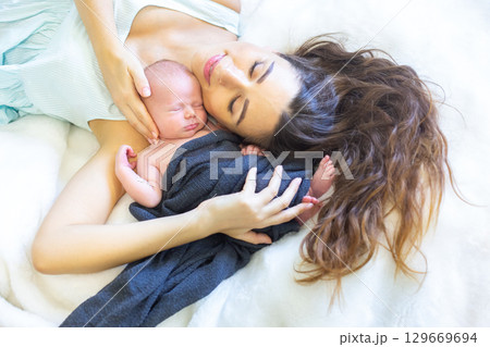 Mother cherishes newborn baby during peaceful moment at home in soft bedding 129669694