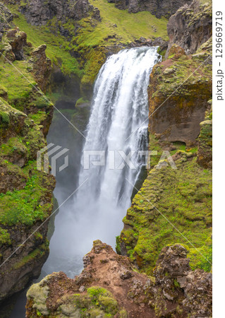 Majestic waterfall cascading through lush cliffs in Iceland's serene landscape Majestic waterfall cascading through lush cliffs in Iceland's serene landscape 129669719