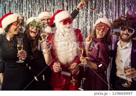 Happy people standing together with a man in Santa Claus costume celebrating New Year's Eve party 129669997