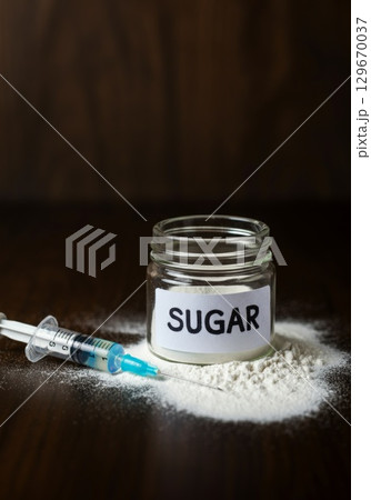 Glass jar labeled sugar with syringe and spilled powder on dark wooden surface 129670037