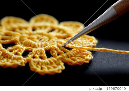 Yellow crochet flower being crafted with a hook on a dark background showcasing intricate details 129670040
