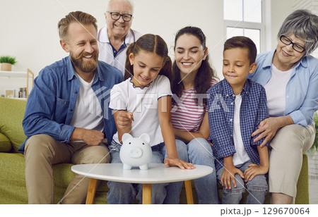 Girl is putting a coin in family white piggy bank while all family is looking at her at home. Girl is putting a coin in family white piggy bank while all family is looking at her at home. 129670064