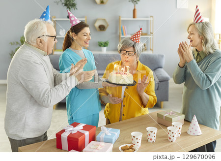 Nurse bringing cake for senior woman celebrating Birthday with aged friends in nursing home. 129670096