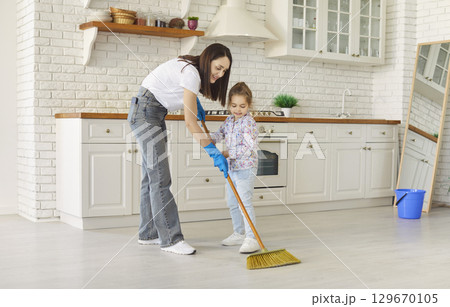Smiling mother with cute daughter sweeping floor with broom in kitchen at home. Smiling mother with cute daughter sweeping floor with broom in kitchen at home. 129670105