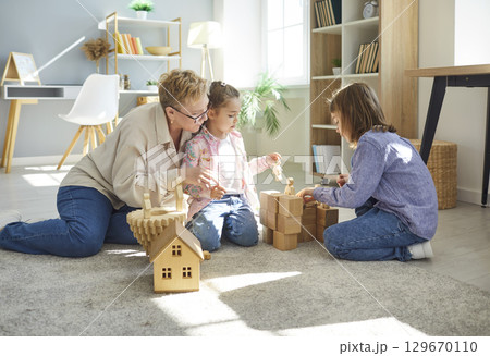 Grandmother playing with her two small granddaughters, building something from wooden blocks 129670110