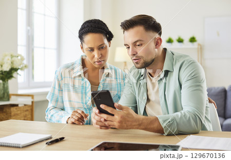 Female and male students gathering together, focused in smartphone, studying 129670136