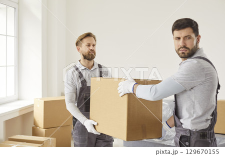 Two movers carrying cardboard boxes from clients house, unload items, dressed in overalls 129670155
