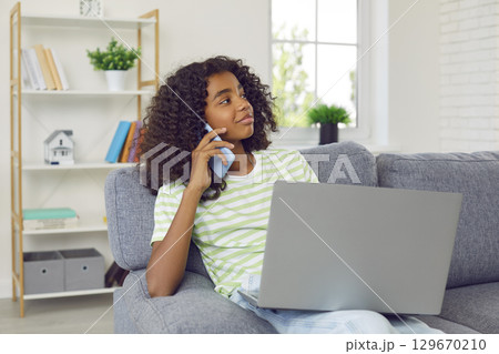 African american teenage girl with laptop sitting in her room and talking on mobile phone. African american teenage girl with laptop sitting in her room and talking on mobile phone. 129670210