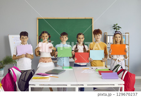 Positive elementary school teens boys and girls in casual clothes show colored paper sheets Positive elementary school teens boys and girls in casual clothes show colored paper sheets 129670237