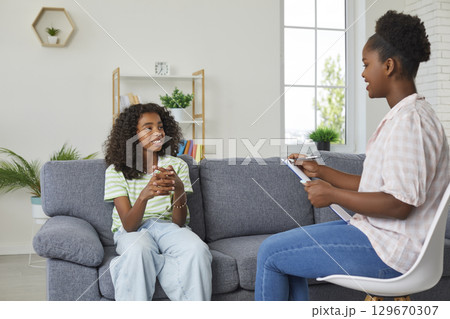 Happy African American girl sitting on couch and talking to her therapist or psychologist 129670307