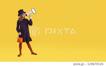 Child in Halloween costume on yellow copy space background making announcement through megaphone 129670326