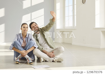 In spacious room, couple sits comfortably on floor and discusses layout of their new home. 129670376