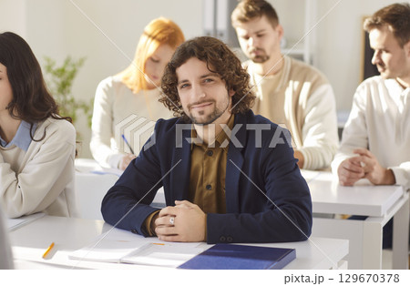 Portrait of smiling university student sitting at desk in classroom during educational lecture. 129670378