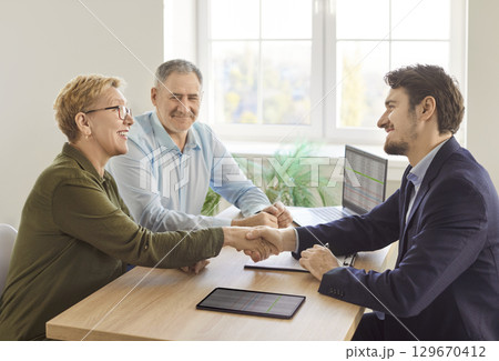 Smiling mature couple shaking hands with business consultant during financial planning meeting. Smiling mature couple shaking hands with business consultant during financial planning meeting. 129670412