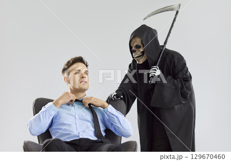 Stressed scared man with person in a Halloween grim reaper death costume holding scythe 129670460