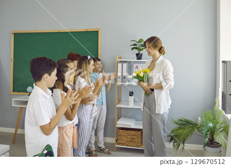 Children students giving flowers to their teacher clapping hands congratulating on holiday. 129670512