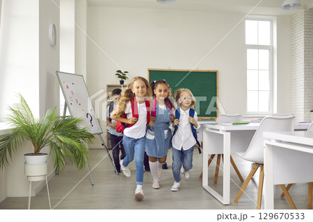 Children dressed in backpacks with textbooks joyfully run out of classroom at end of lessons. 129670533
