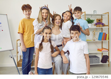 Cheerful little students making horns with their fingers and their friendly young teacher. 129670546