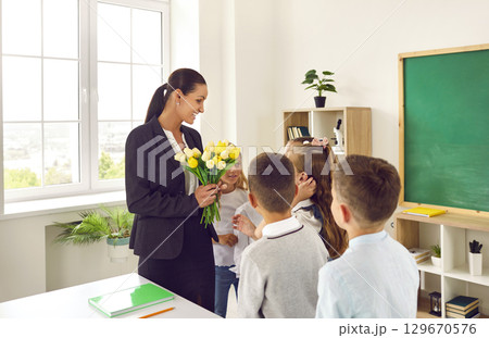 Little children congratulate their beloved woman teacher and give flowers stand in school room Little children congratulate their beloved woman teacher and give flowers stand in school room 129670576