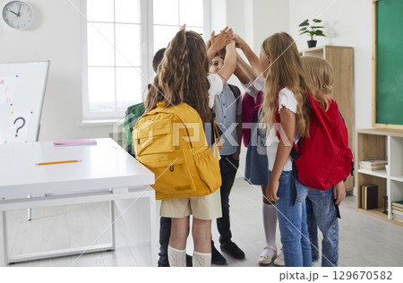 Group of school children with backpacks standing in circle and joining their hands Group of school children with backpacks standing in circle and joining their hands 129670582