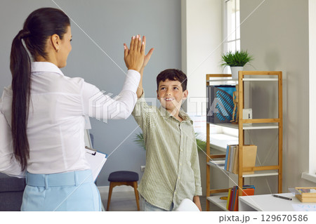 Happy little boy gives a high five to his psychologist after a successful therapy session Happy little boy gives a high five to his psychologist after a successful therapy session 129670586